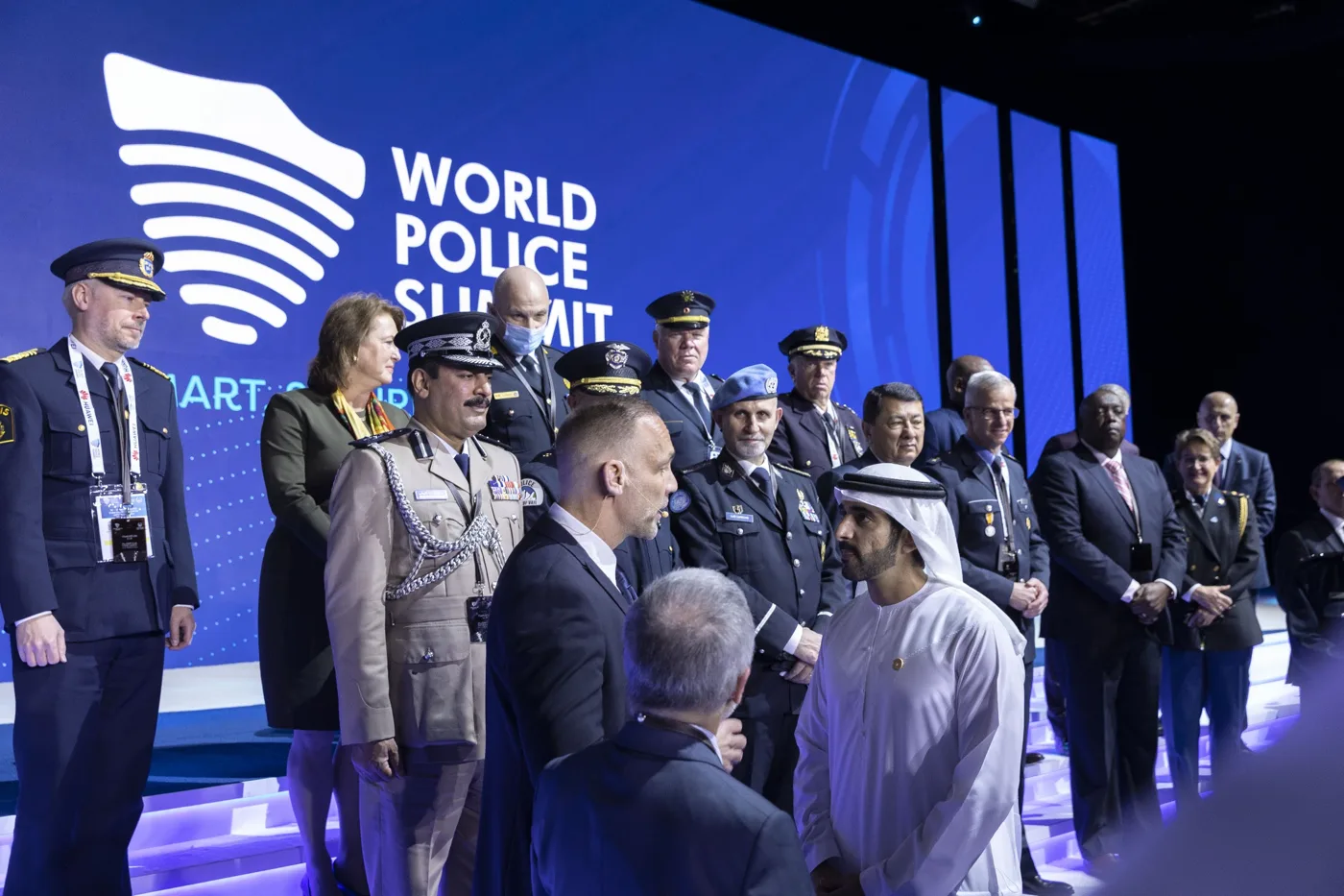 Groepsfoto op het podium van de World Police Summit, met politiemensen in uniform voor het scherm met de naam van de summit